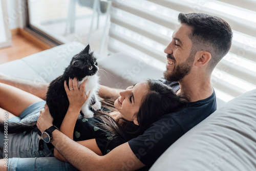 Obraz na płótnie Happy couple spending leisure time with cat while sitting at home w salonie