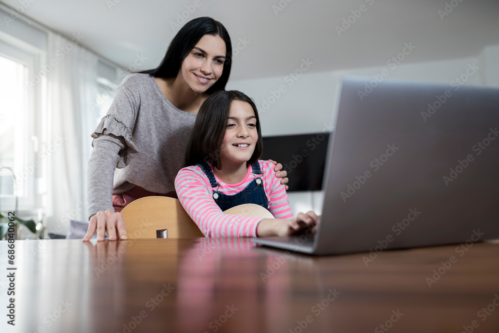 Mother and daughter smiling in front of laptop with daughter holding a guitar Mother and daughter smiling in front of laptop with daughter holding a guitar