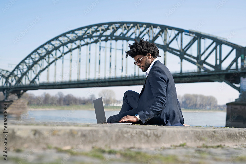Businessman sitting at the riverside using laptop