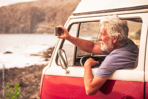 Senior man travelling in a vinatge van, taking pictures of the sea photo