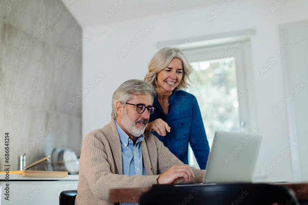 Mature man with wife using laptop on kitchen table at home Mature man with wife using laptop on kitchen table at home