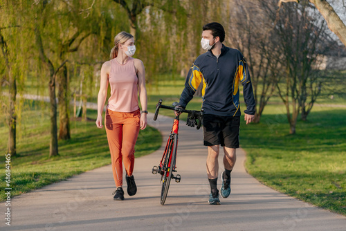 Young couple walking with bicycle on footpath at park during coronavirus pandemic