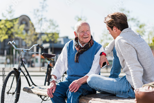 Senior man and adult grandson talking on a bench photo