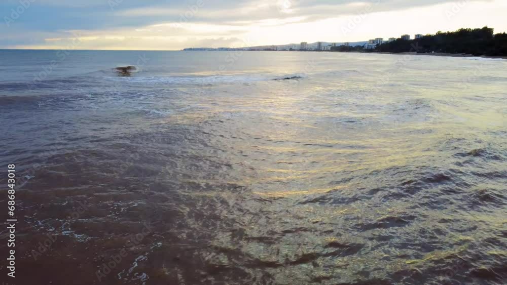 Drone flies over water as waves roll onto shore at seaside town. Water at seaside town coast, drone captures sunset serenity. Water meets shore in seaside town, drone view of tranquil water at sunset Drone flies over water as waves roll onto shore at seaside town. Water at seaside town coast, drone captures sunset serenity. Water meets shore in seaside town, drone view of tranquil water at sunset