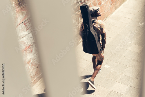 Young man walking in the city, carrying guitar case