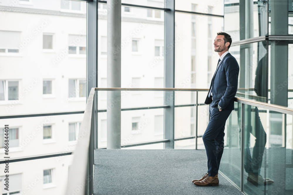 Successful businessman standing in office building, looking out of window, daydreaming Successful businessman standing in office building, looking out of window, daydreaming