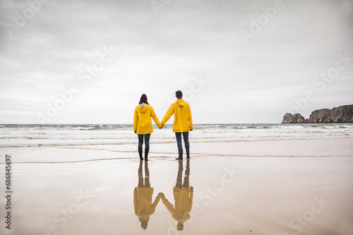 Young woman wearing yellow rain jackets and standing at the beach, Bretagne, France photo