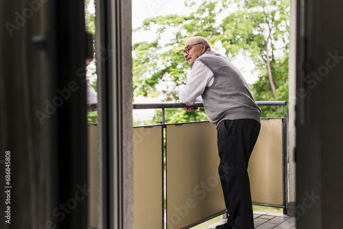 Curious senior man standing on balcony watching something photo