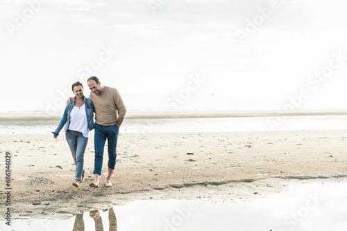 Obraz na płótnie Smiling mature couple walking at beach against sky during sunset w salonie