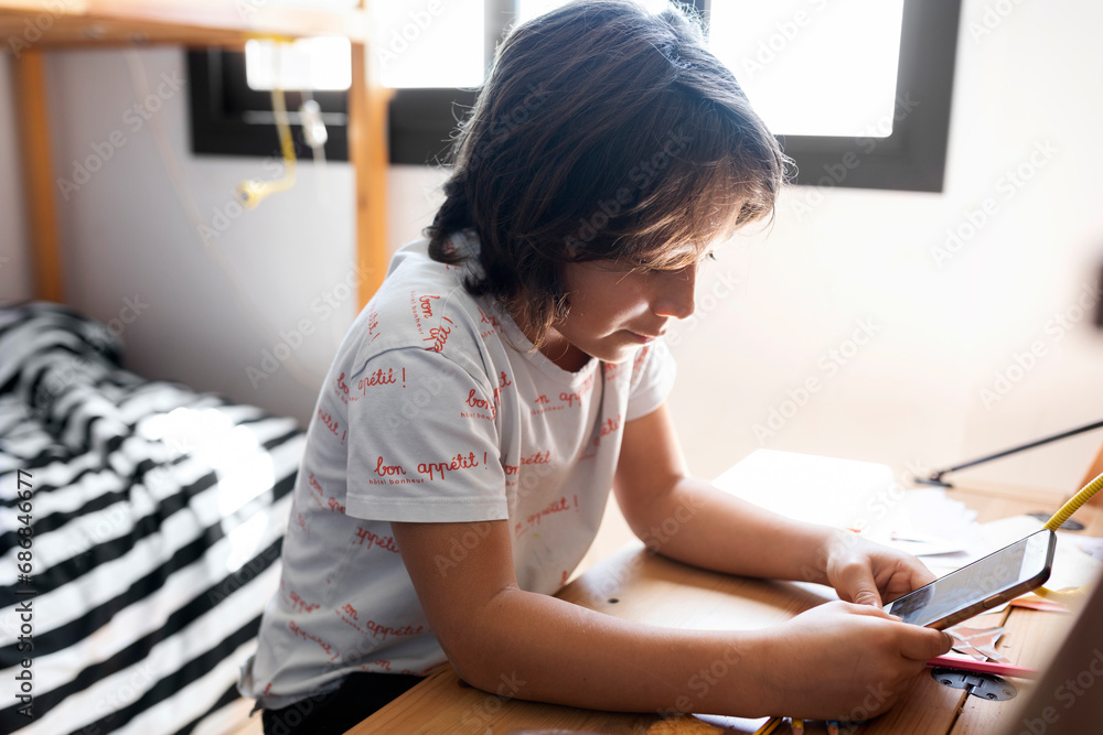 Boy sitting at desk at home using smartphone Boy sitting at desk at home using smartphone