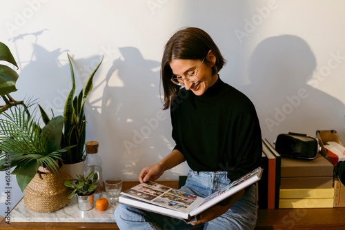Smiling woman looking photographs in photo album while sitting at home