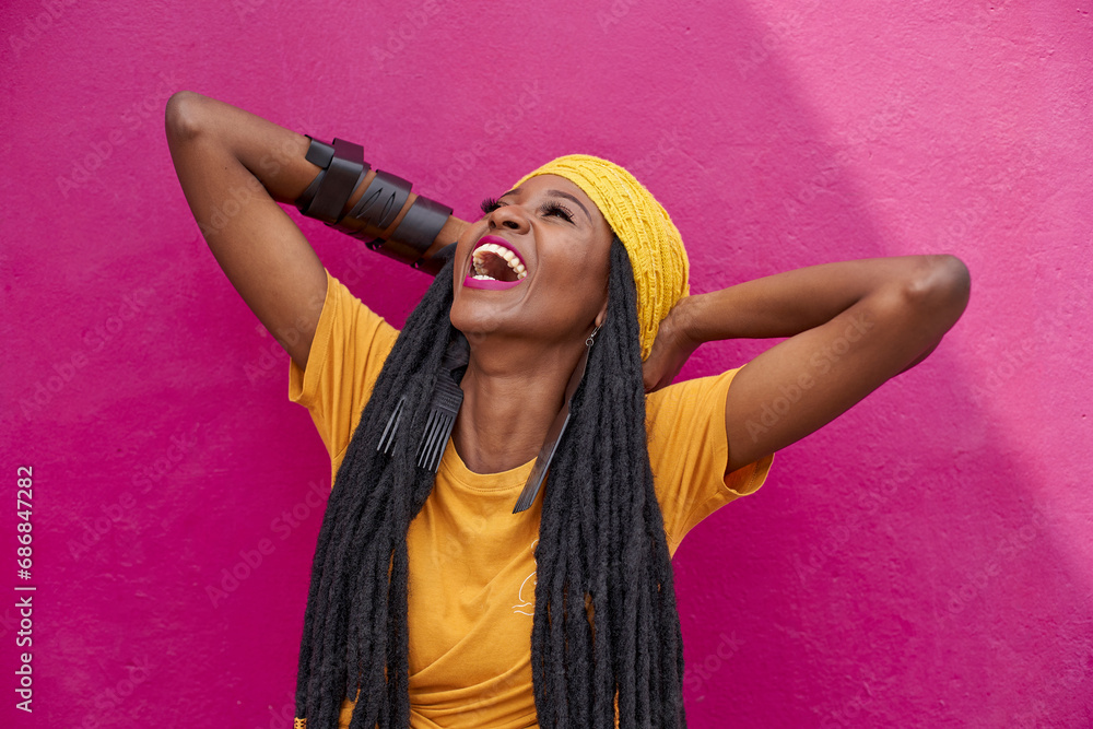 Portrait of woman with long dreadlocks laughing in front of a pink wall - obrazy, fototapety, plakaty 