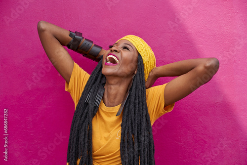 Portrait of woman with long dreadlocks laughing in front of a pink wall photo
