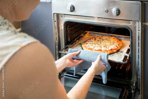 Crop view of woman taking tray with baked pizza out of oven