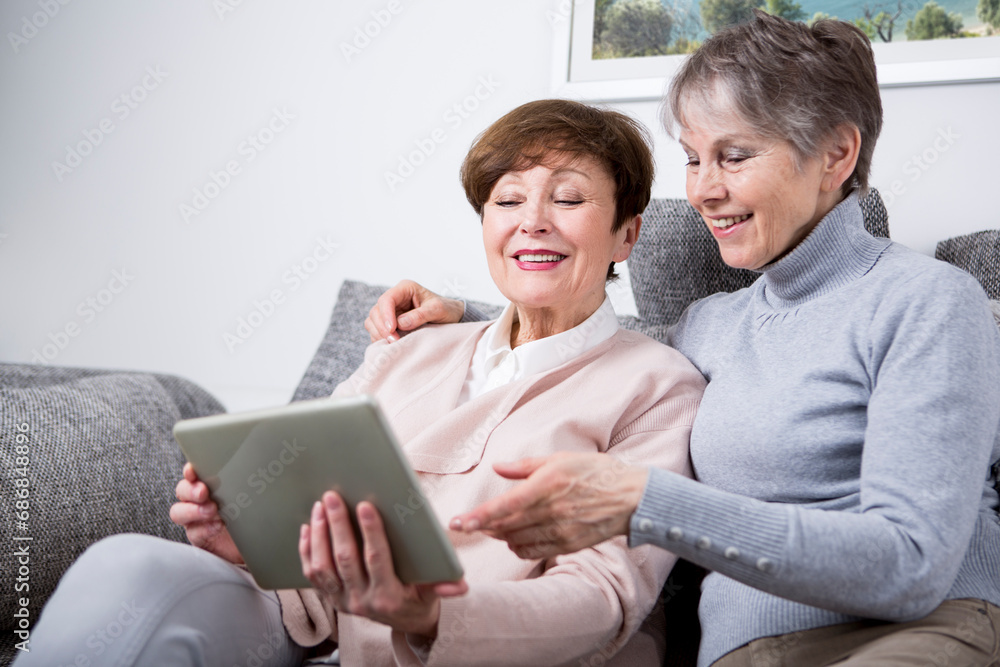 Two senior women sitting on couch, looking at digital tablet Two senior women sitting on couch, looking at digital tablet