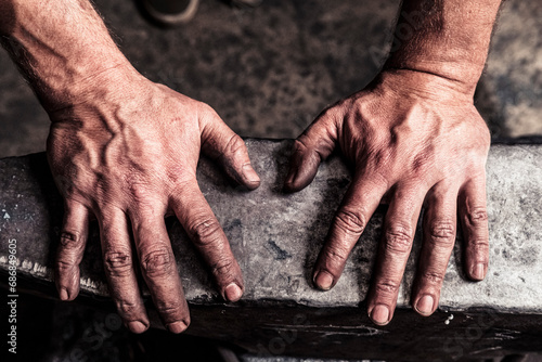 Knife maker with soot-blackened hands on anvil