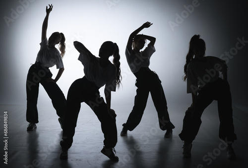 In the shot on a black background in the light of a spotlight in the silhouette. Dance group consisting of attractive girls. They show dance moves towards jazz funk. photo