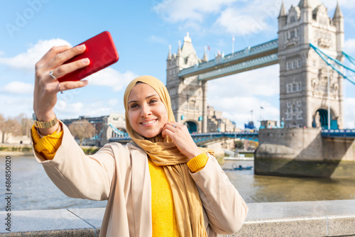 Photography Portrait of smiling young woman taking selfie with smartphone in front of Tower