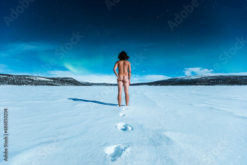 Nude man standing in winter landscape watching northern lights above Ropijarvi, Ropinsalmi, Enontekioe, Finland #686850204