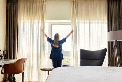 Chambermaid opening curtains of window in hotel room photo