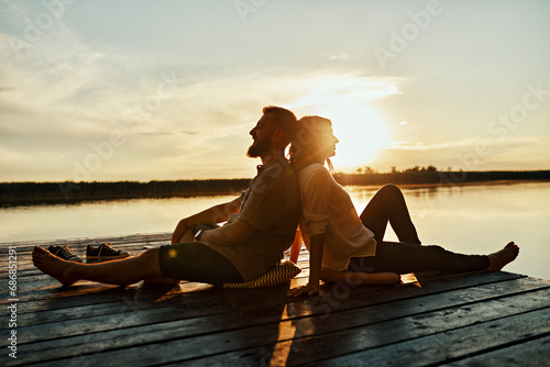 Couple sitting back to back on jetty at a lake at sunset photo
