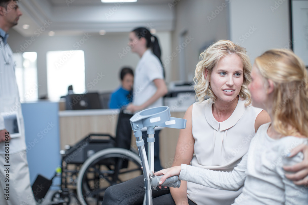 Girl with crutches sitting with her mother in reception area