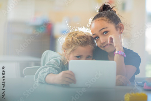 Portrait of two smiling girls sharing mini tablet in kindergarten photo