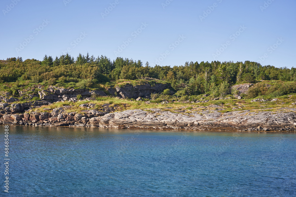 Beautiful and wild scandinavian coast in Norway with polar or tundra type countyside, rocks, dwarfed trees, blueberry bushes and heather. Picture is taken from the water during sunny summer afternoon.