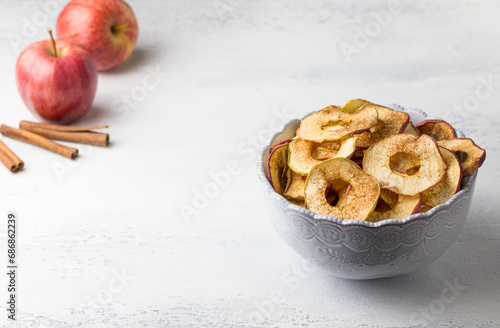 Homemade dried apples with cinnamon, apple chips in a bowl with cinnamon sticks on a light gray background. Delicious healthy snack