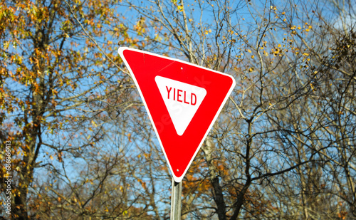 yield sign on road, symbolizing caution and giving way to oncoming traffic, against a clear blue sky