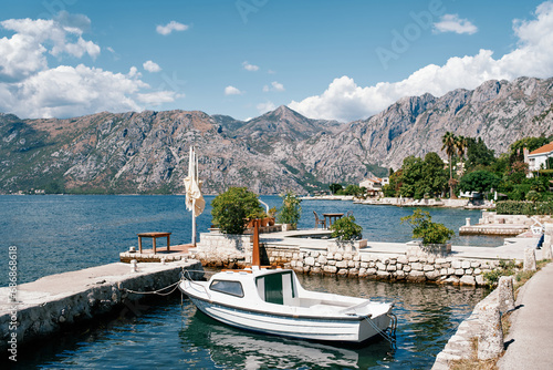 Small boat is moored at the stone pier of an ancient town at the foot of the mountains. Dobrota, Montenegro