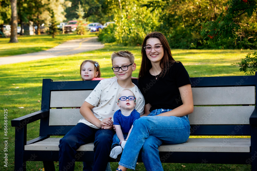 Portrait of four sibilings enjoying quality time together in a city park, during a warm fall afternoon and the youngest boy has Down Syndrome; Leduc, Alberta, Canada Portrait of four sibilings enjoying quality time together in a city park, during a warm fall afternoon and the youngest boy has Down Syndrome; Leduc, Alberta, Canada