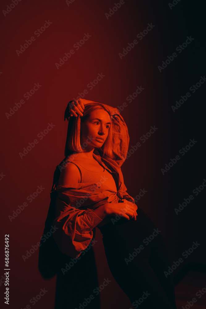 Fashion-forward woman posing in a red glow, her artistic expression captured in a modern studio setting