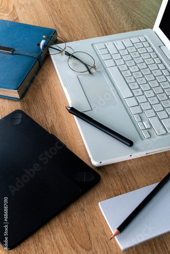 white laptop on a wooden table with blue agenda and graphic tablet, glasses on a white laptop, work and study space, graphic design photo