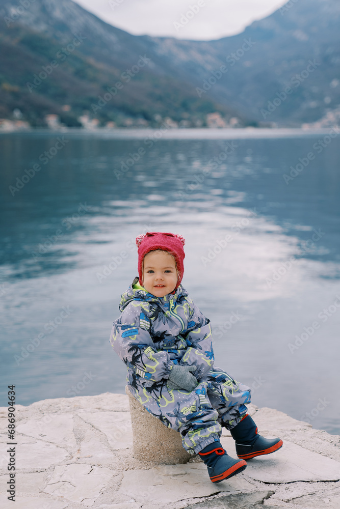 Little smiling girl sitting on a bollard on the pier