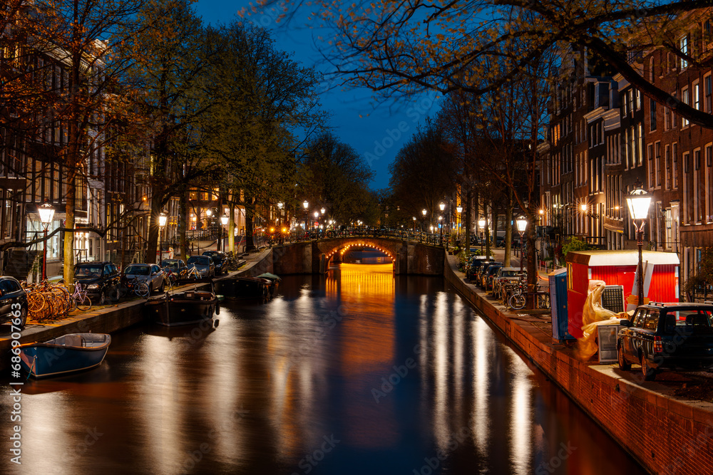 Long exposure photography capturing a mesmerizing night scene along the Amsterdam canal. The colorful lights reflecting on the serene water create a captivating and peaceful cityscape.