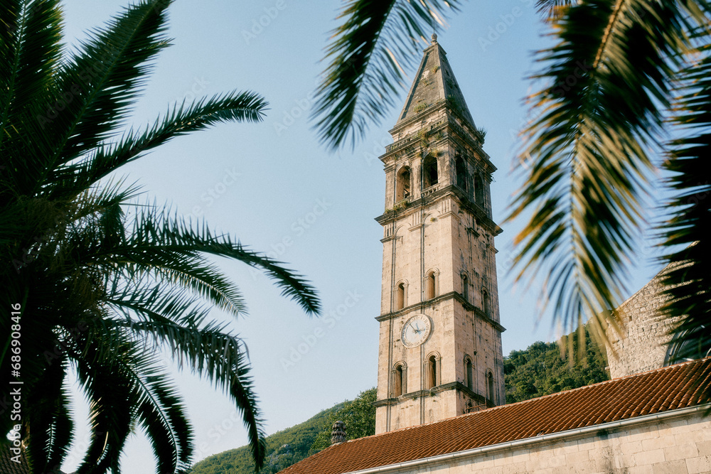 View through palm branches to the high bell tower of the Church of St. Nicholas. Perast, Montenegro