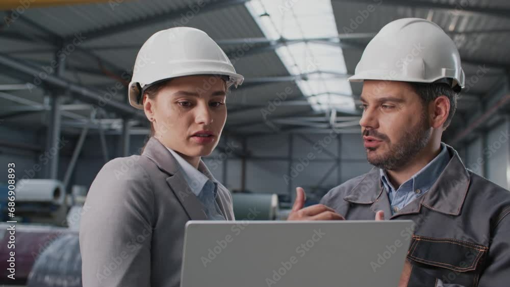 Hardworking Caucasian people with helmets talking with each other while working on laptop. Young workers discussing about future buildings in their factory. Developing industrial business. Hardworking Caucasian people with helmets talking with each other while working on laptop. Young workers discussing about future buildings in their factory. Developing industrial business.