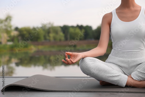 Woman practicing Padmasana on yoga mat outdoors  closeup and space for text. Lotus pose