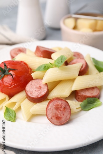 Tasty pasta with smoked sausage, tomato and basil on table, closeup