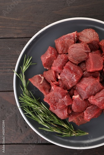 Pieces of raw beef meat with rosemary on wooden table, top view