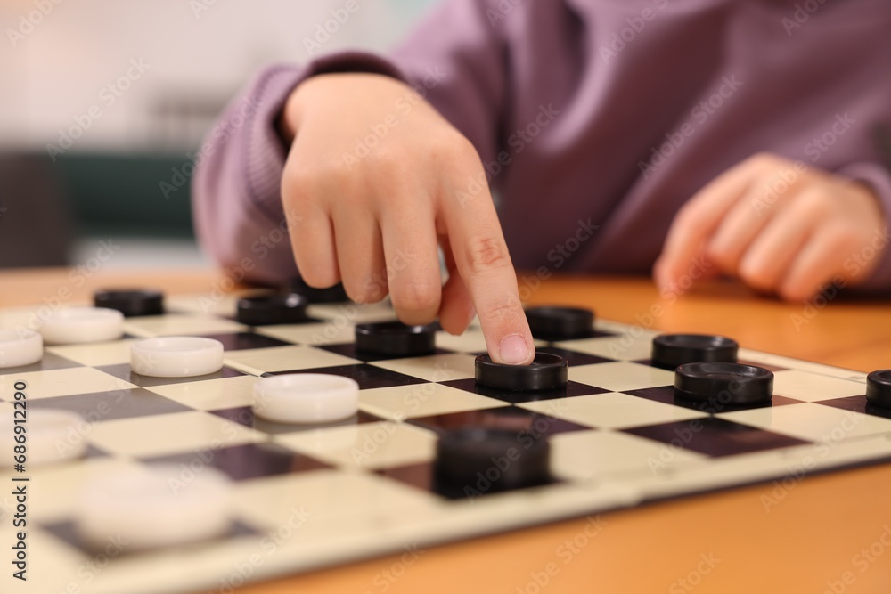 Boy playing checkers at wooden table indoors, closeup