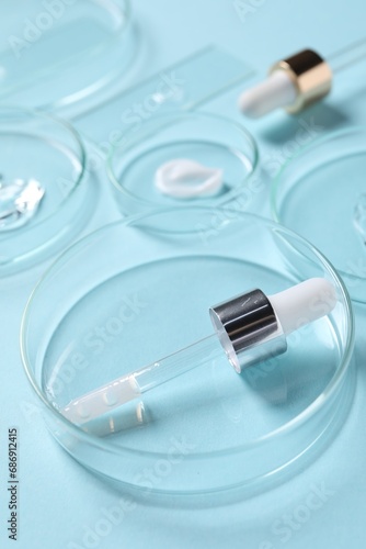 Petri dishes with cosmetic serums and pipettes on light blue background, closeup