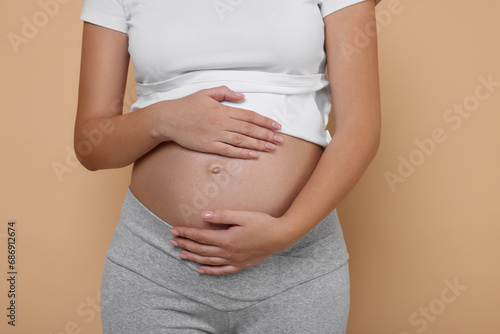 Pregnant woman in white T-shirt on beige background, closeup © New Africa