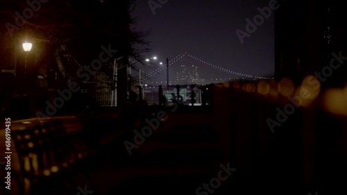 Brooklyn promenade at night with partial view of Verrazano Bridge in background.