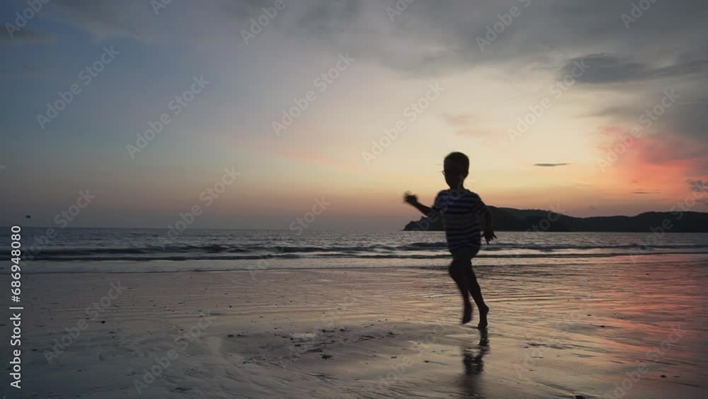 Little boy is running along a sand beach at sunset Little boy is running along a sand beach at sunset