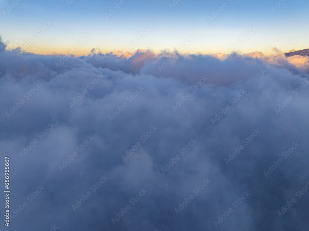 Fototapeta premium Aerial view of flowing fog waves on mountain tropical rainforest,Bird eye view image over the clouds Amazing nature background with clouds and mountain peaks in indonesia