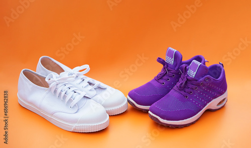 Two pairs of white and purple canvas sneakers. Orange background. Comfortable, fashionable. Concept, shoes for doing sport or exercise also can wear for traveling, hiking. 