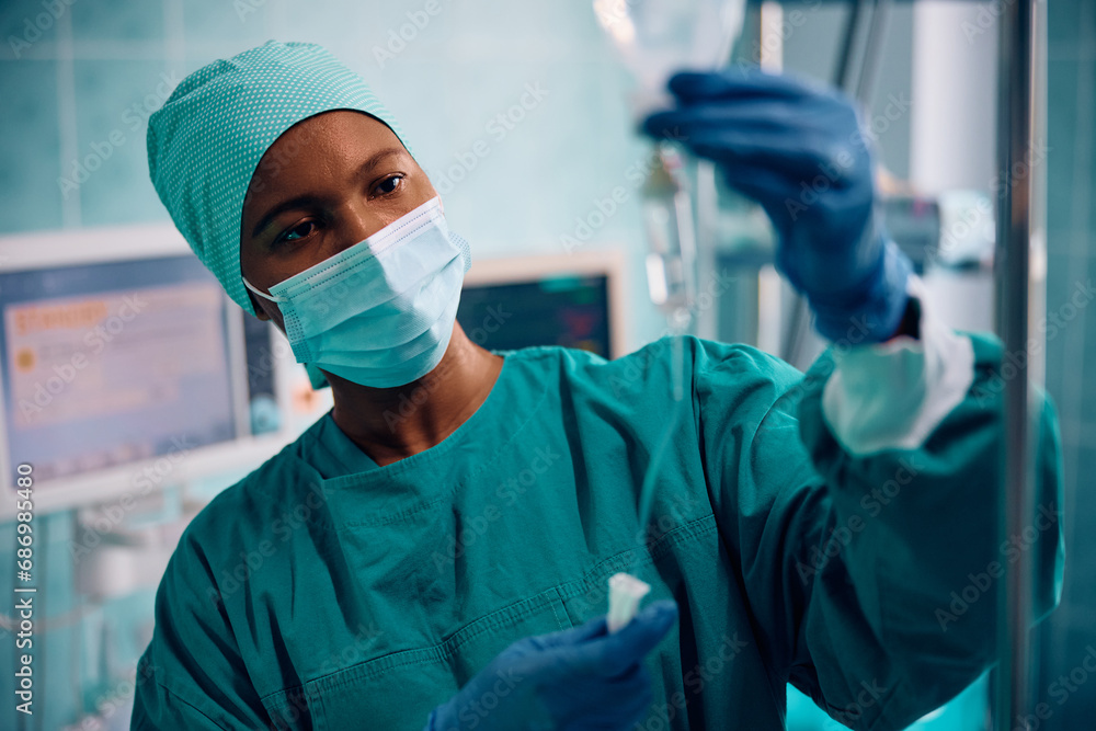 Black female nurse checking IV drip in operating room in hospital. Black female nurse checking IV drip in operating room in hospital.