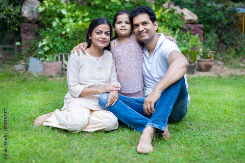 Happy indian family sitting in the park or garden. Young parent with cute little daughter.
